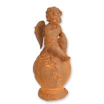 A RUSTY CAST IRON FIGURINE OF A PUTTO SITTING ON BALL